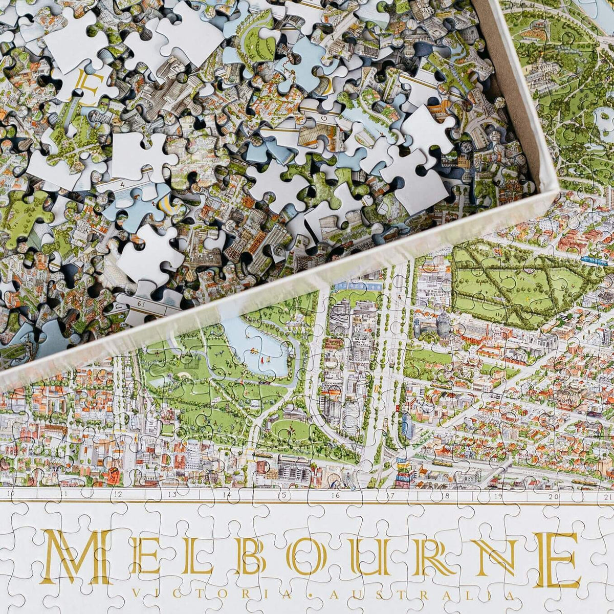 The Melbourne Map 1,000-piece jigsaw puzzle. The image shows a close up of the &quot;Melbourne&quot; name title and the surrounding detail and in the top left corner is the open box with loose pieces. 