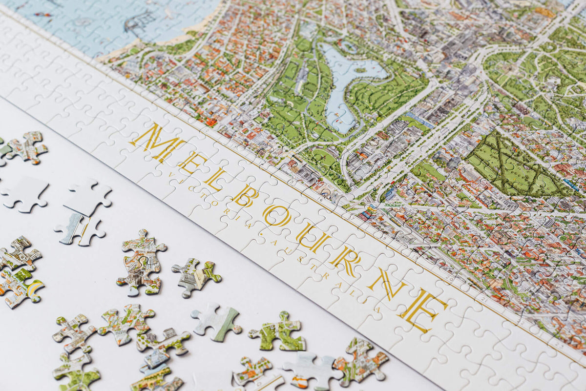 The Melbourne Map 1,000-piece jigsaw puzzle on a white board. The image shows the completed puzzle on a diagonal and some loose piece next to it. 