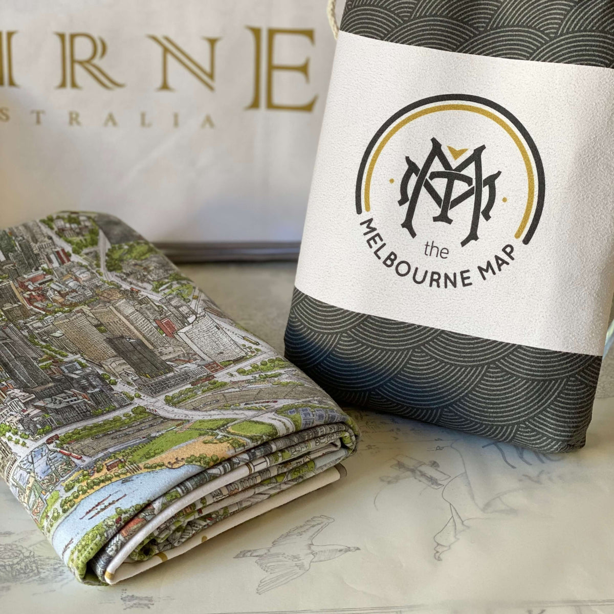 The Melbourne Map Beach Towel folded next to its bag showing how lightweight and compact it is. 