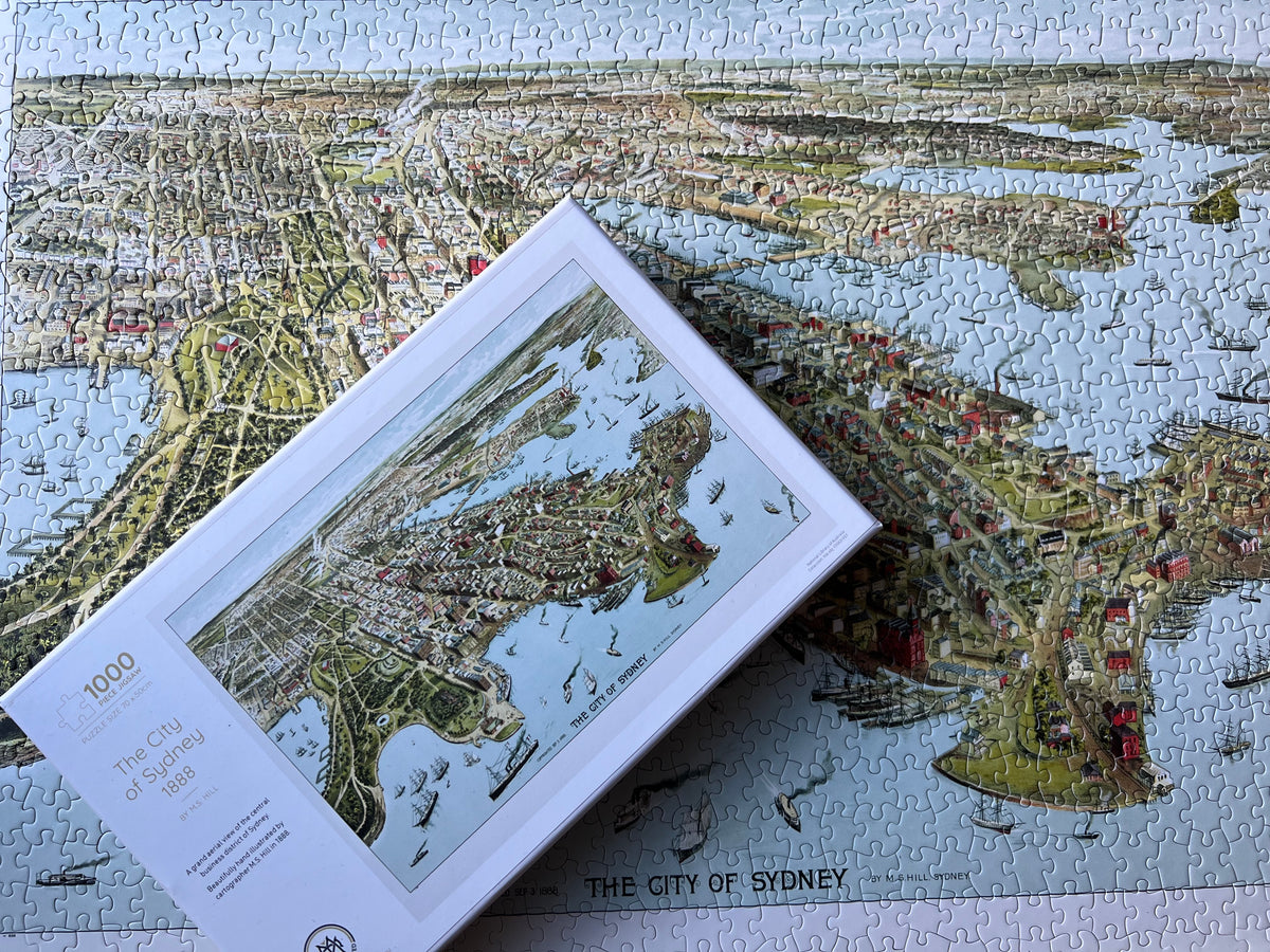 Photo of a completed jigsaw of the city of Sydney with the box on top of the jigsaw