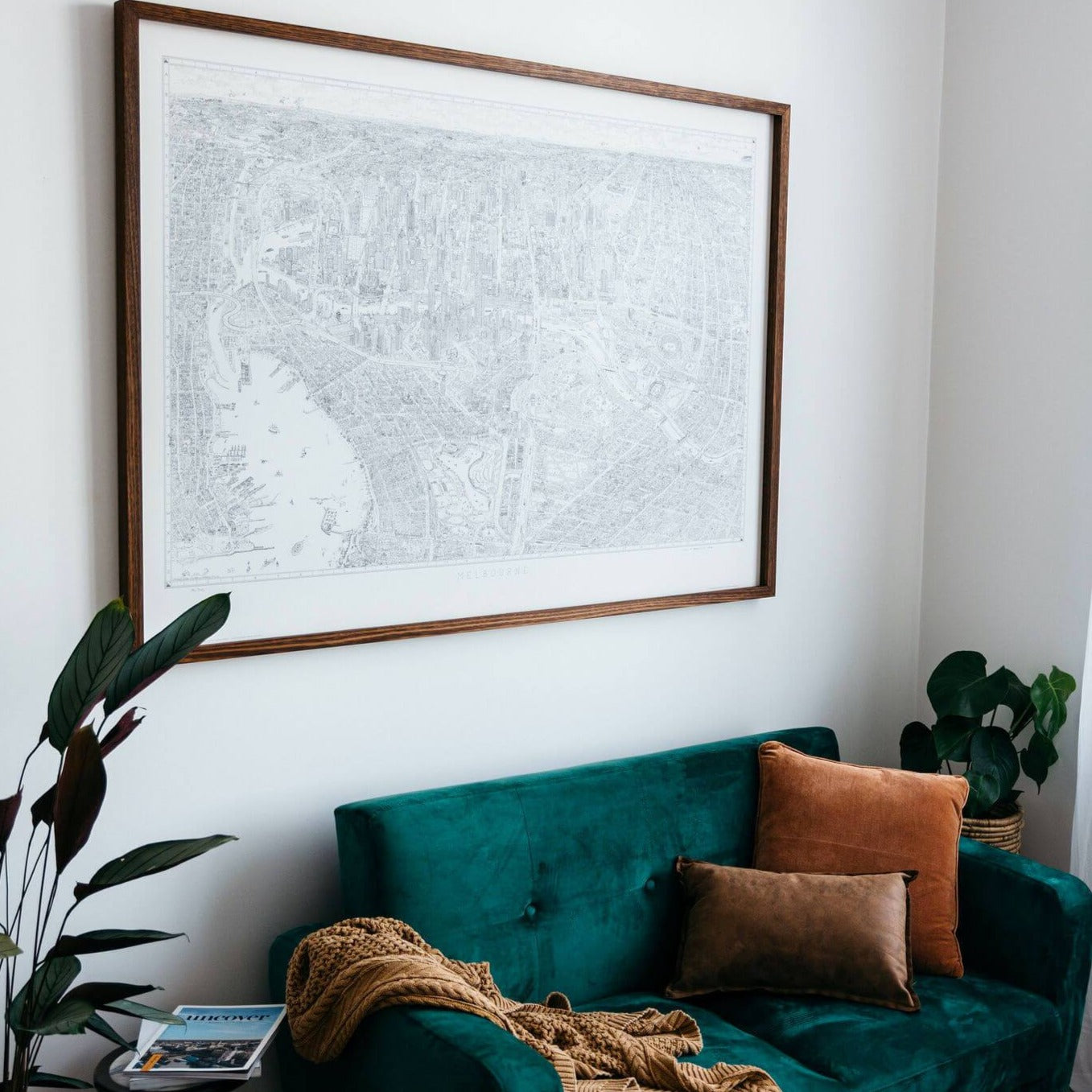A copy of The Melbourne Map Limited Edition of 300 line drawing framed in stained Victorian Ash. The print is hanging above a small green velvet sofa in a bright airy room
