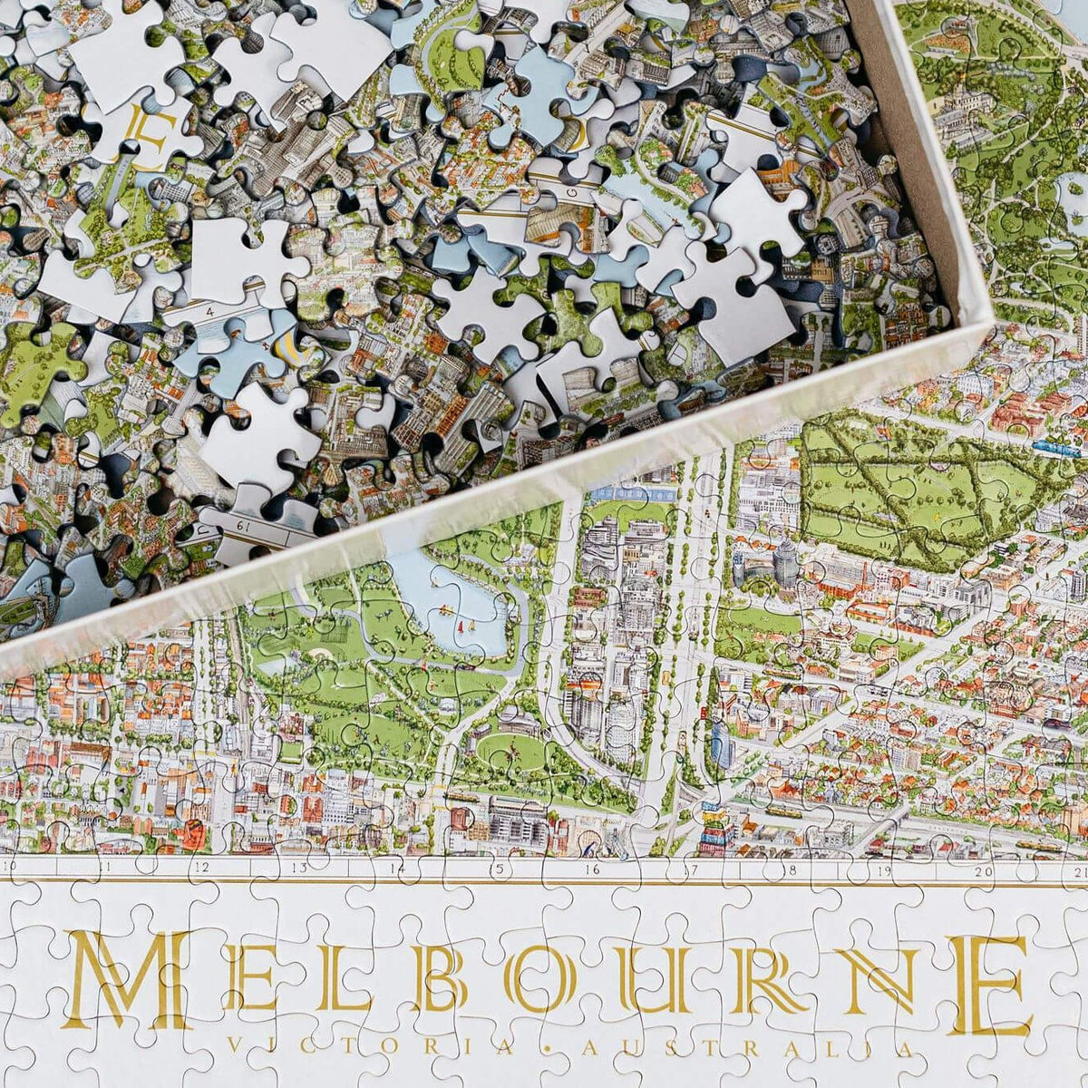 The Melbourne Map 1,000-piece jigsaw puzzle. The image shows a close up of the &quot;Melbourne&quot; name title and the surrounding detail and in the top left corner is the open box with loose pieces.