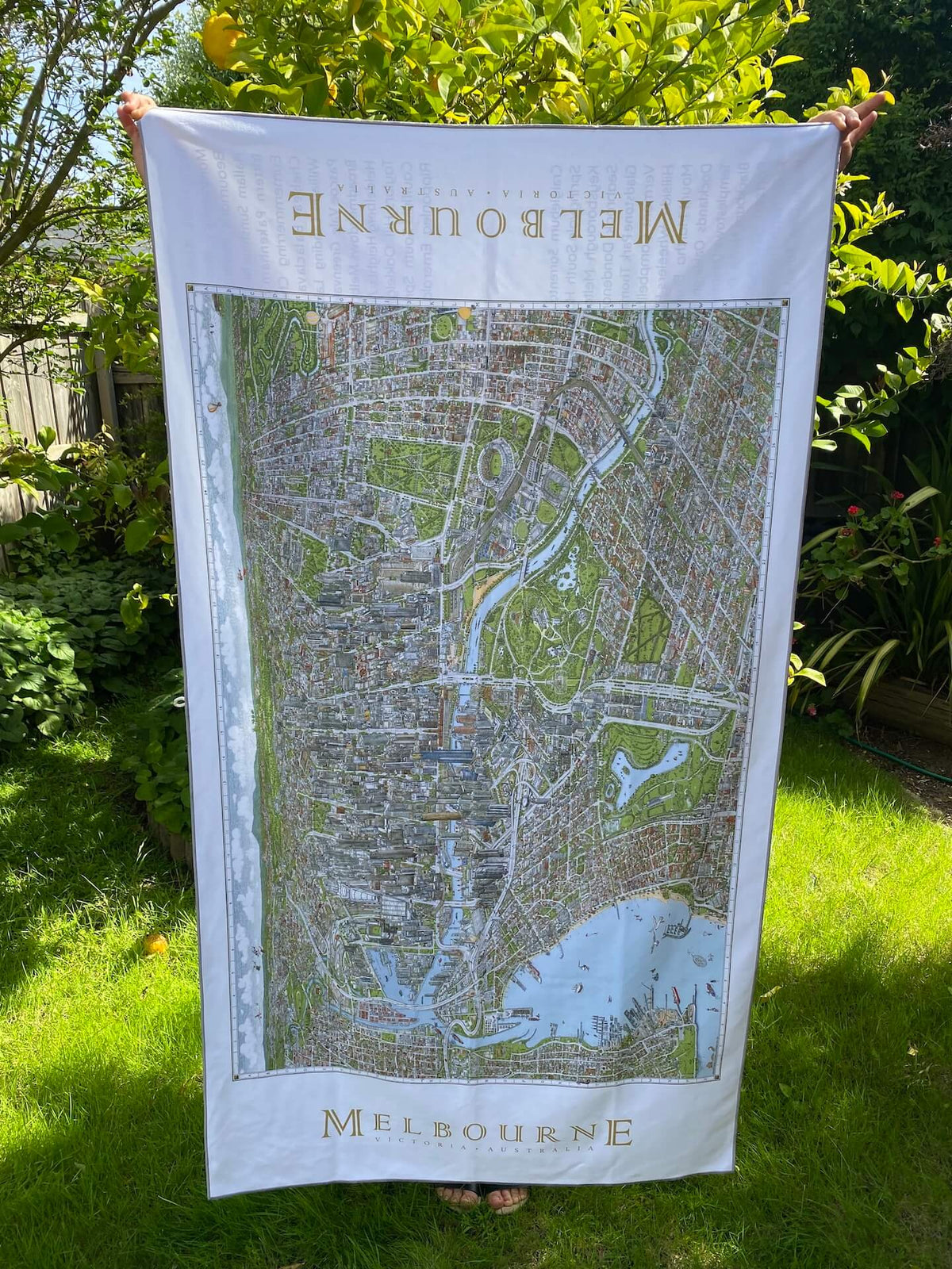 Mel holding up The Melbourne Map Beach Towel to show size and scale of the image in the garden of our beautiful Drysdale studio. Lemon tree in the background. 