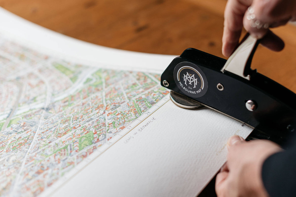 Melinda Clarke hand embossing a limited edition colour print of The Melbourne Map showing the quality of the archival paper used and the detail of the drawing