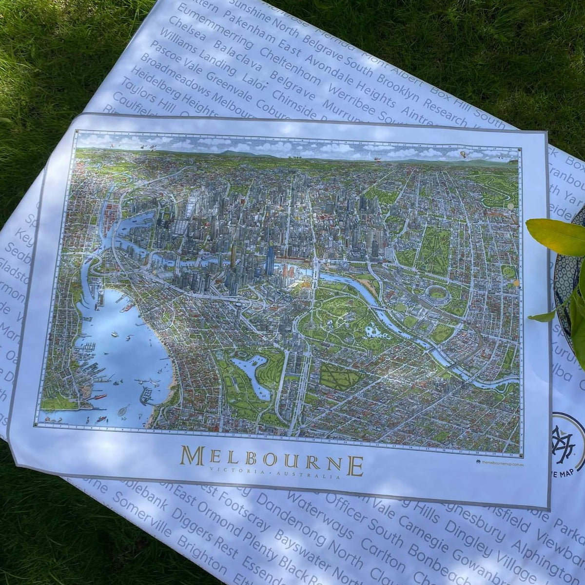 The Melbourne Map Tea Towel laid flat on top of the beach towel showing the whole map image. 